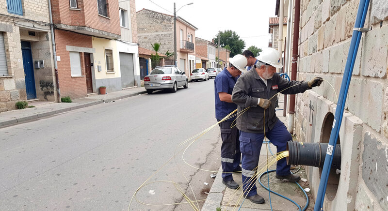 Technicians pulling fiber optic cable through an open conduit on a small town street.