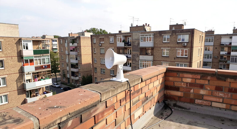 A small white directional antenna mounted on a brick apartment rooftop overlooking a residential block.